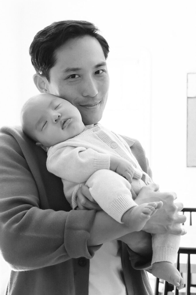 Black and white photo of a father holding his newborn son as he sleeps.