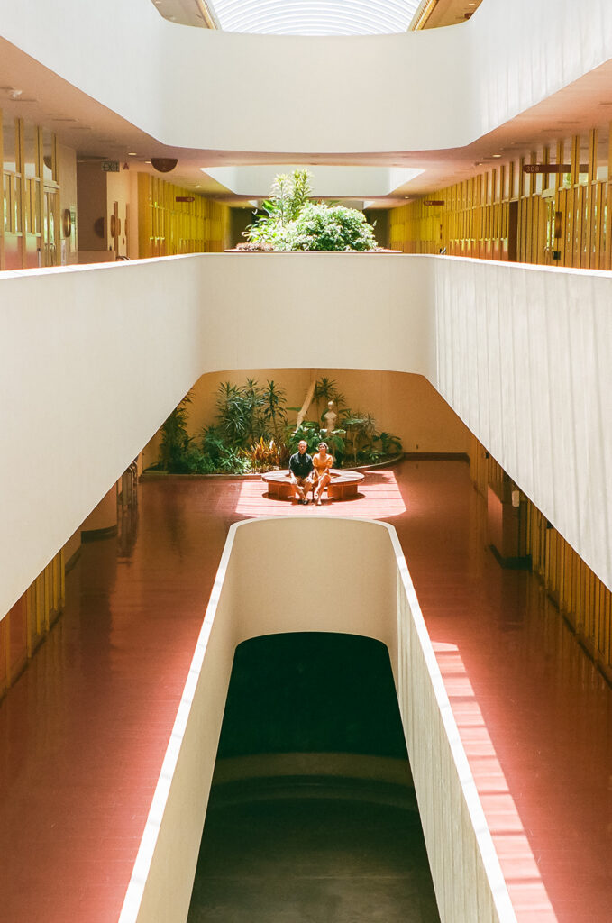 Couple sitting together inside Marin County Civic Center for colorful film-inspired Bay Area engagement photos.