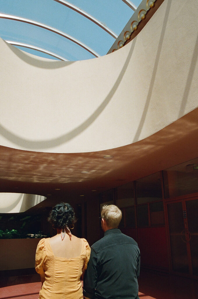 Couple sitting together inside Marin County Civic Center for colorful film-inspired Bay Area engagement photos.