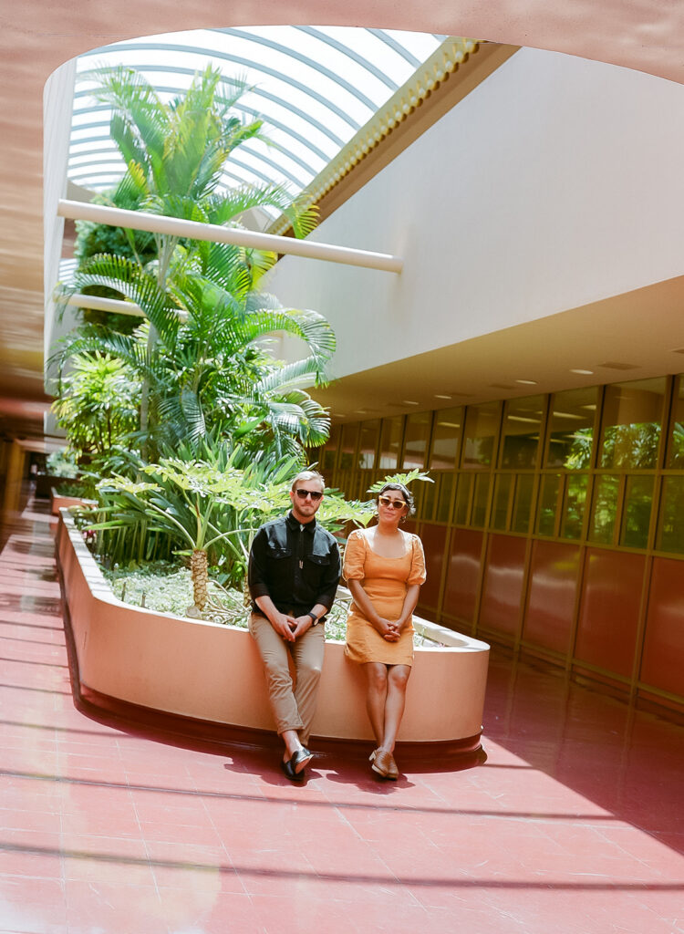 Couple sitting together inside Marin County Civic Center for colorful film-inspired Bay Area engagement photos.