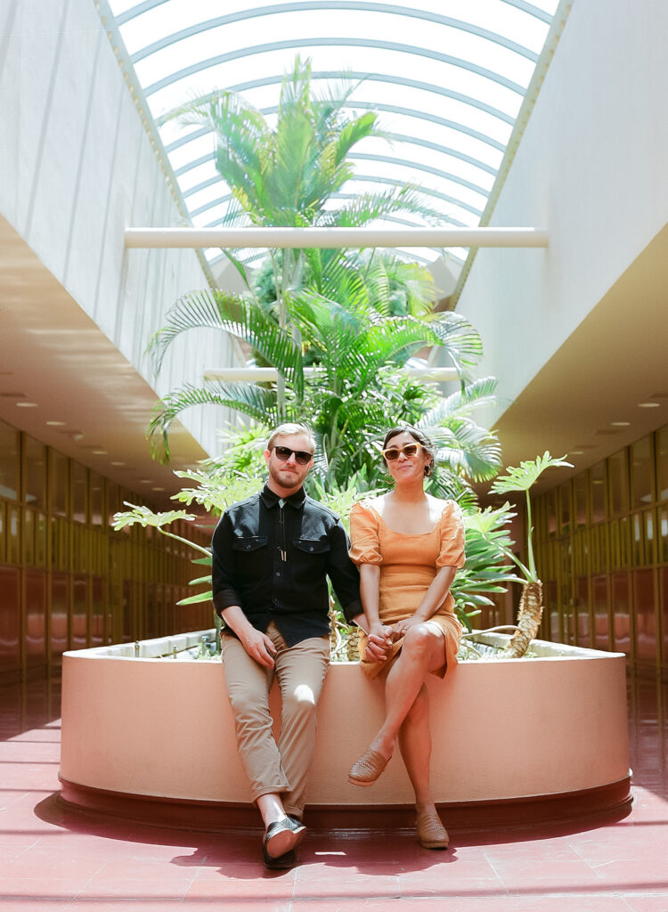 Couple sitting together inside Marin County Civic Center for colorful film-inspired Bay Area engagement photos.