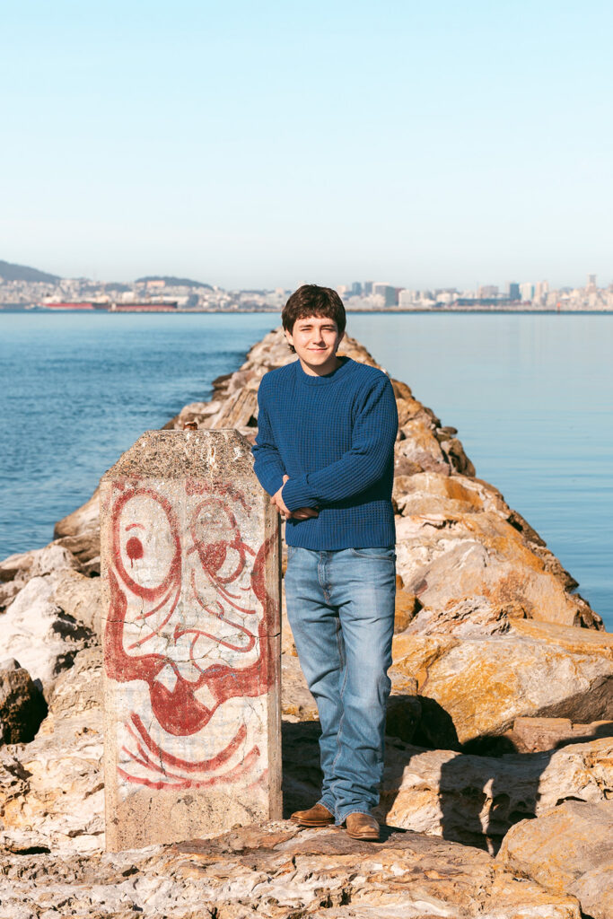 Senior portrait beside a graffiti-covered concrete marker and rocks along the Alameda waterfront.
