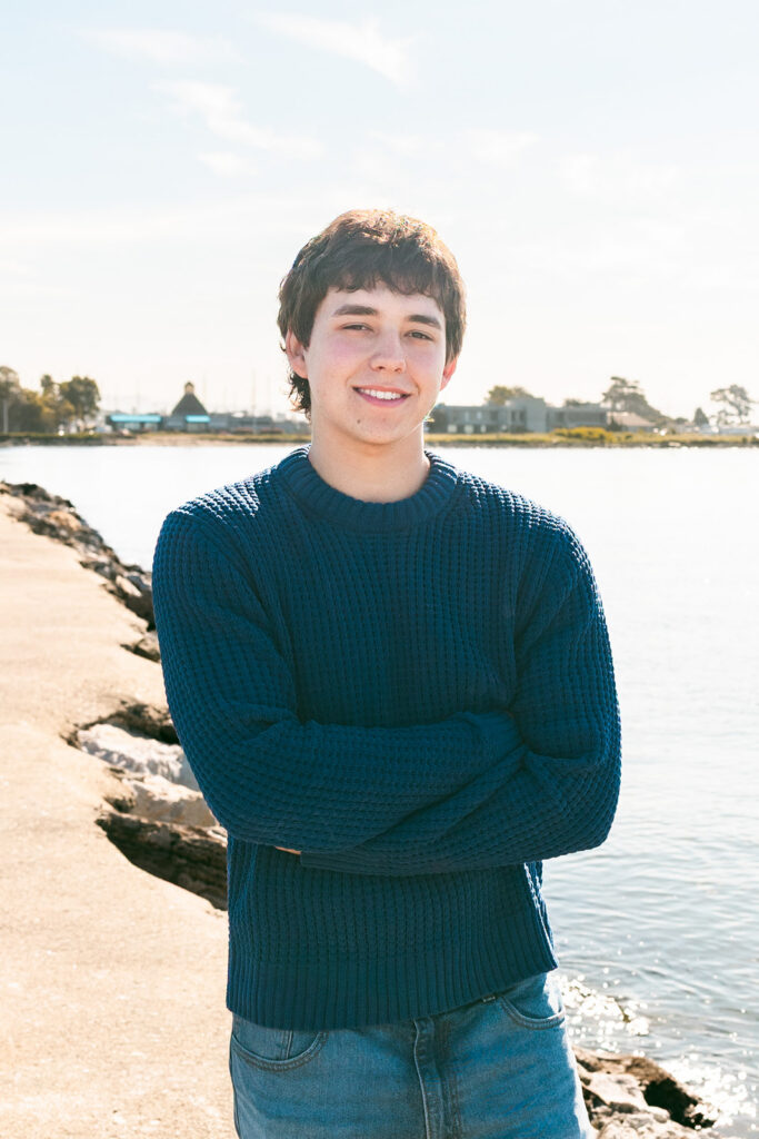 Close-up senior portrait in a blue sweater beside the water at the Alameda Rock Wall.