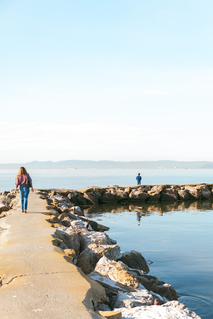 Senior standing at the end of the Alameda Rock Wall as his mother walks toward him along the waterfront path.