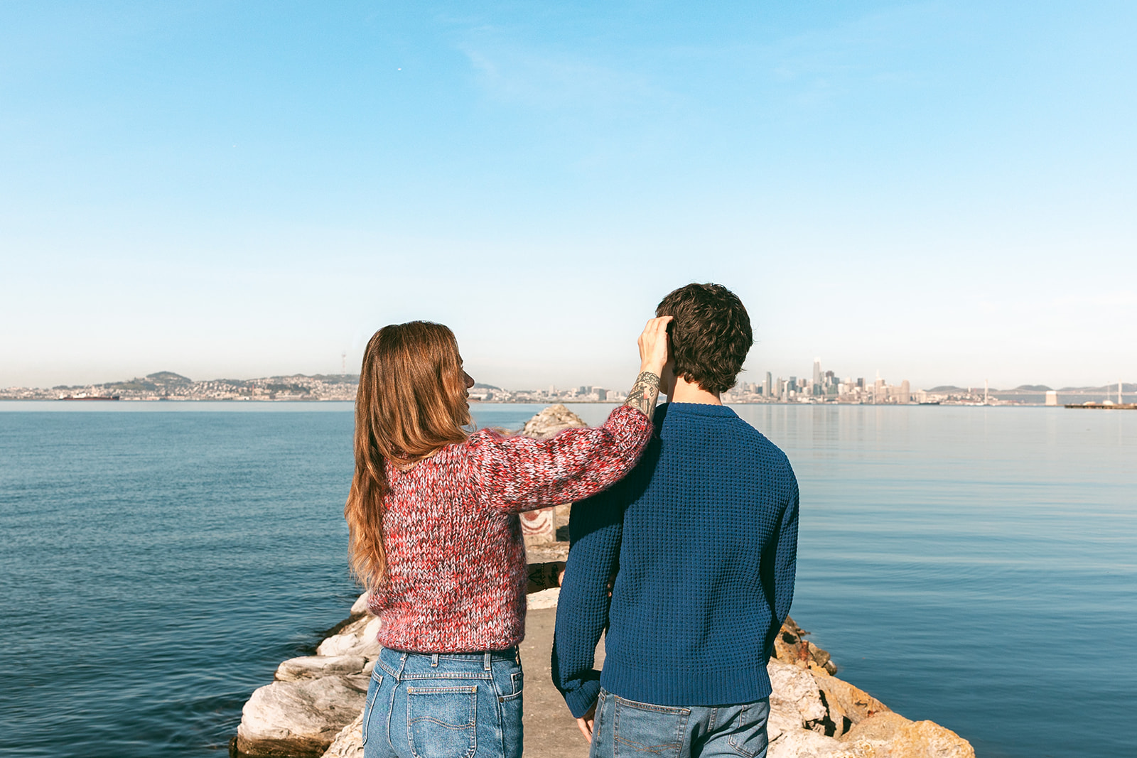 Candid photo of a mom adjusting her son’s hair at the Alameda Rock Wall with the San Francisco skyline in the background.