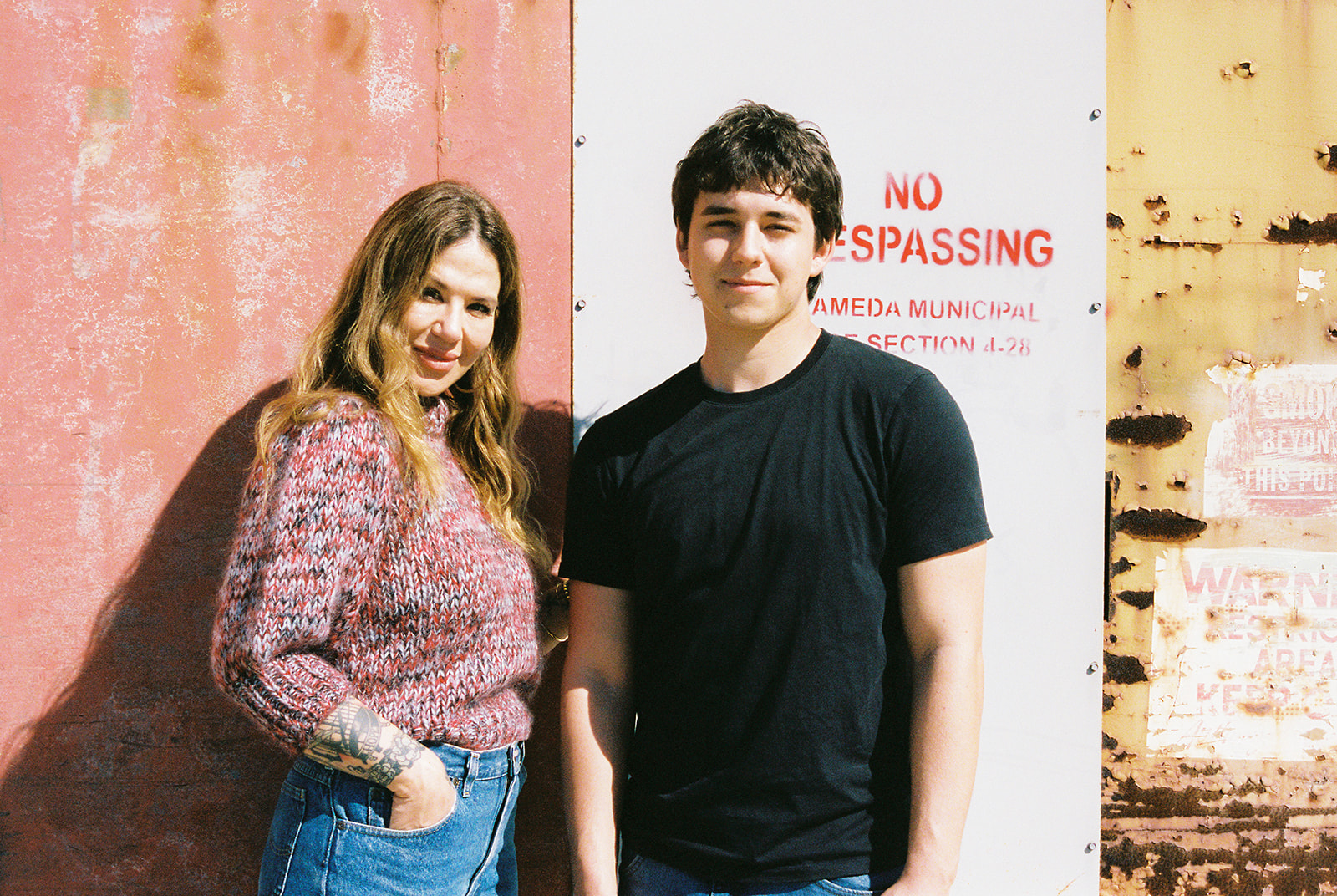 Film portrait of a senior and his mom together against a colorful weathered hangar at the former Alameda Naval Air Station.