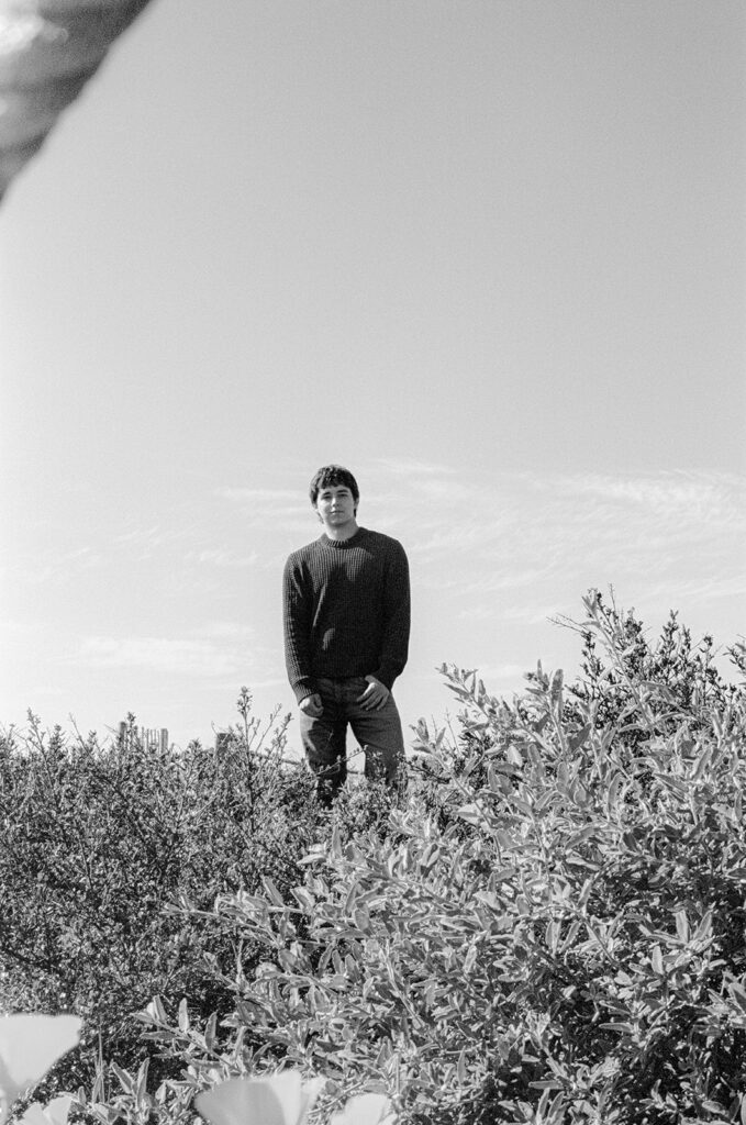 Black and white film senior portrait standing among coastal plants in Alameda.