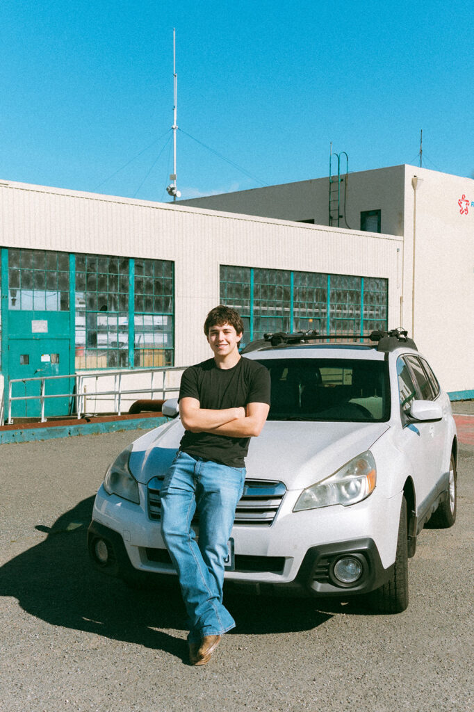 Senior leaning against his car outside an industrial building at the former Naval Air Station in Alameda.