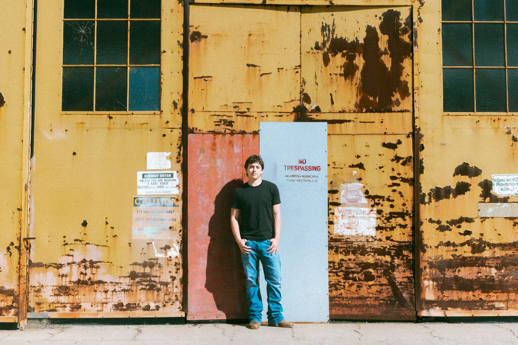 Senior standing in front of a colorful rusted hangar door during an Alameda senior portrait session.