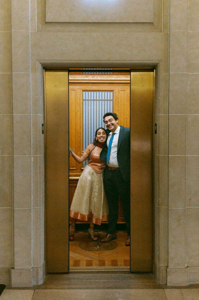 Smiling couple standing together in a vintage elevator at San Francisco City Hall.