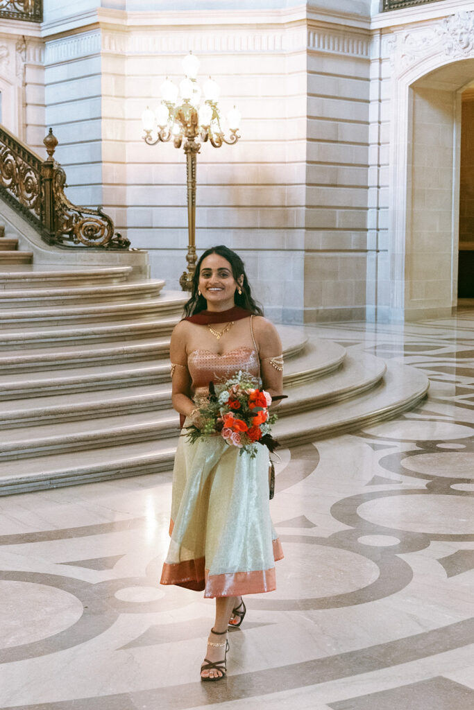 Bride holding a colorful bouquet near the grand staircase at San Francisco City Hall.