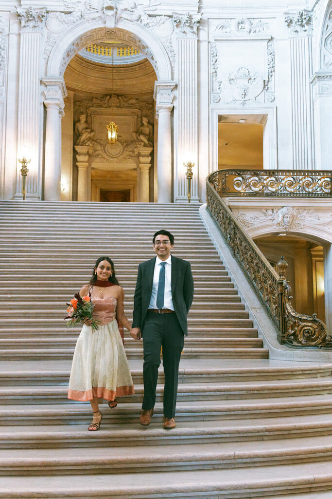 Bride and groom walking down the marble staircase at San Francisco City Hall.