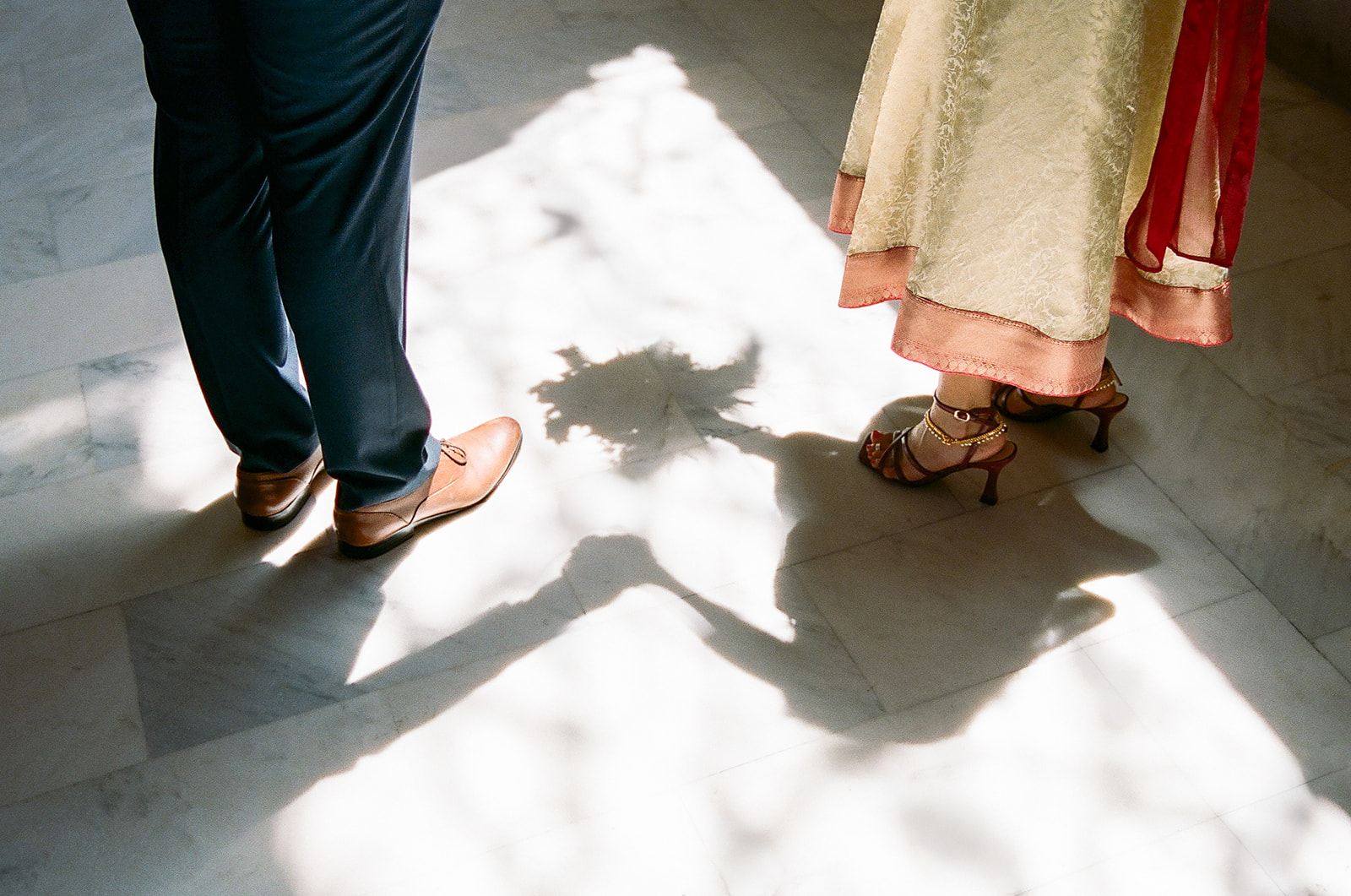 Bride and groom holding hands with their shadows cast across the marble floor.