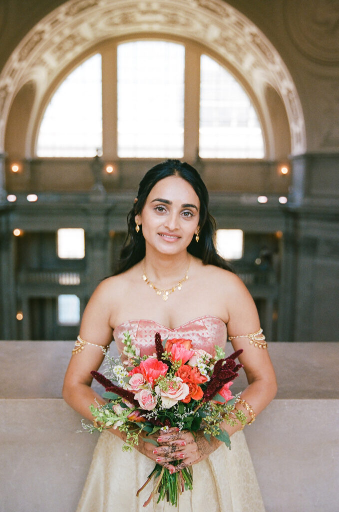 Bride holding a colorful bouquet in front of the large arched windows at San Francisco City Hall.