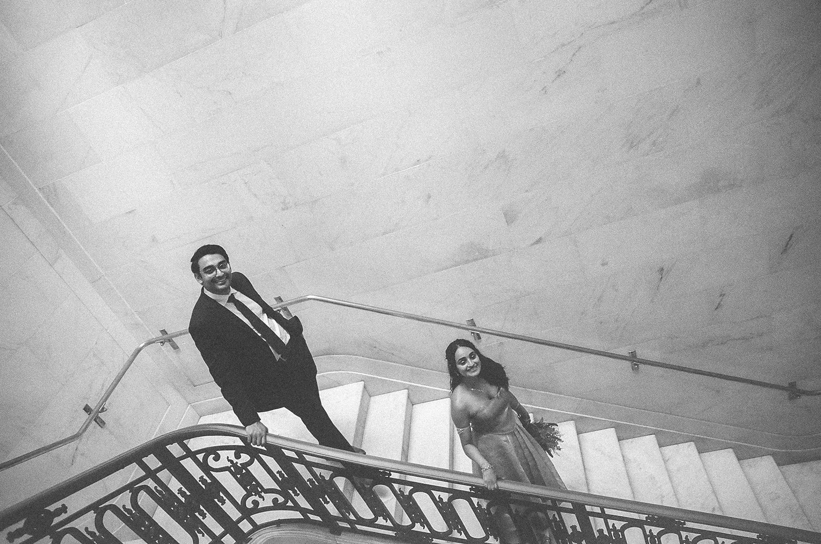 Black and white film photo of a couple walking down the stairs at San Francisco City Hall.
