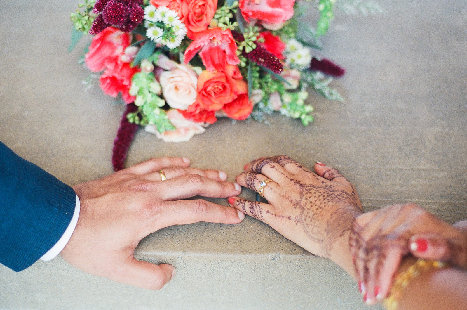 Close up shot of a couples hands touching with their weddings rings and the brides bouquet.