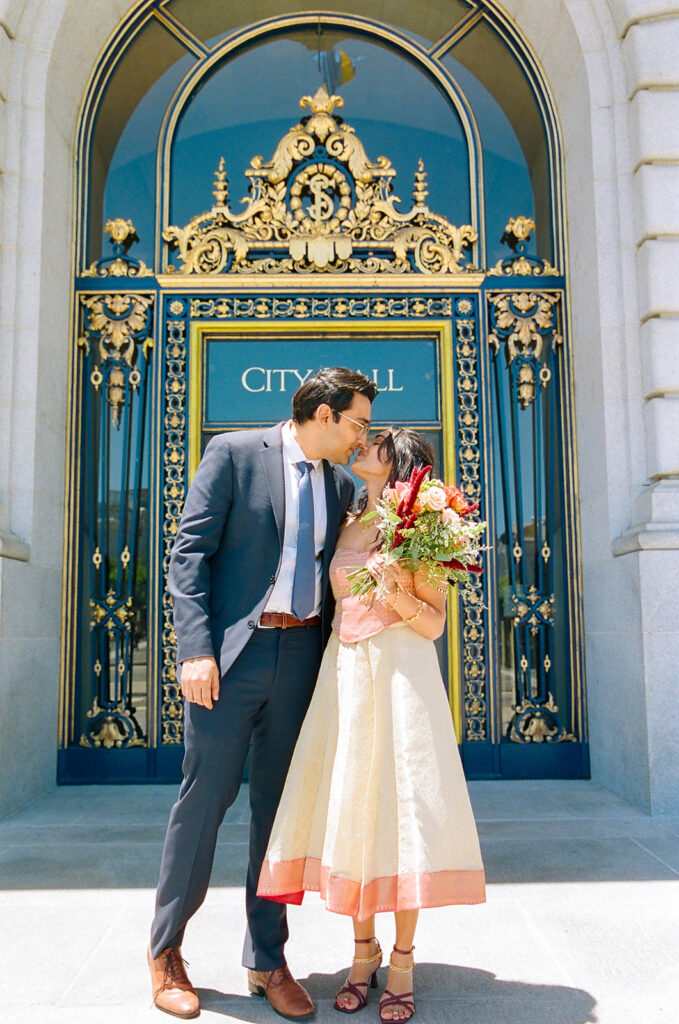 Bride and groom kissing in front of the ornate entrance to San Francisco City Hall.