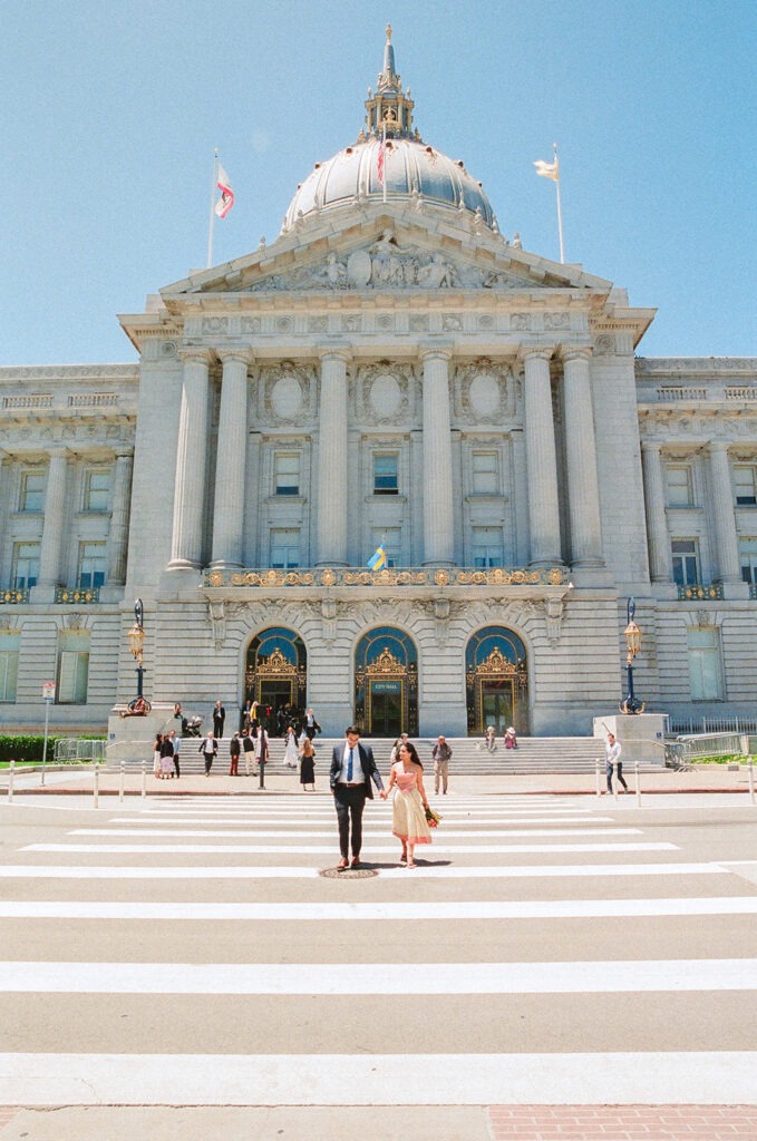 Newlyweds walking outside with the San Francisco City Hall building behind them.