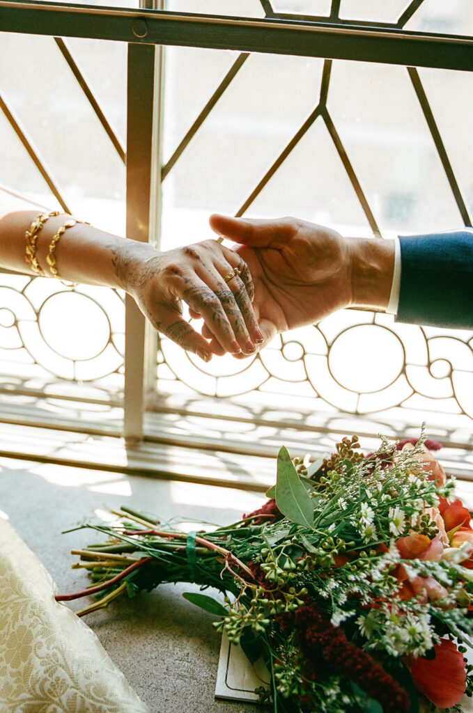 Close-up of the newlyweds holding hands beside a colorful wedding bouquet.