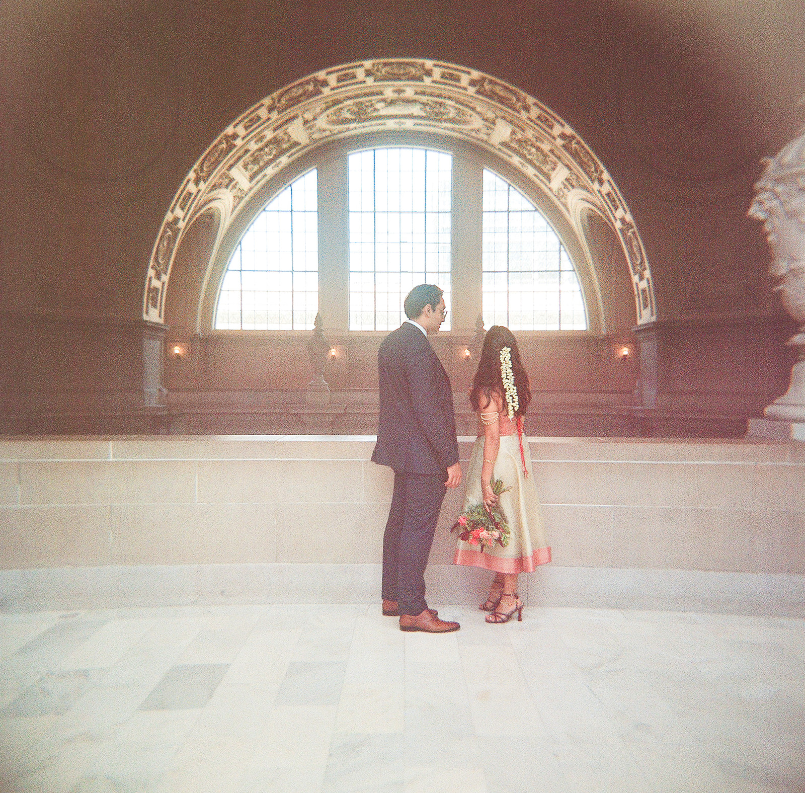 Bride and groom standing beneath a large arched window during their San Francisco City Hall wedding.
