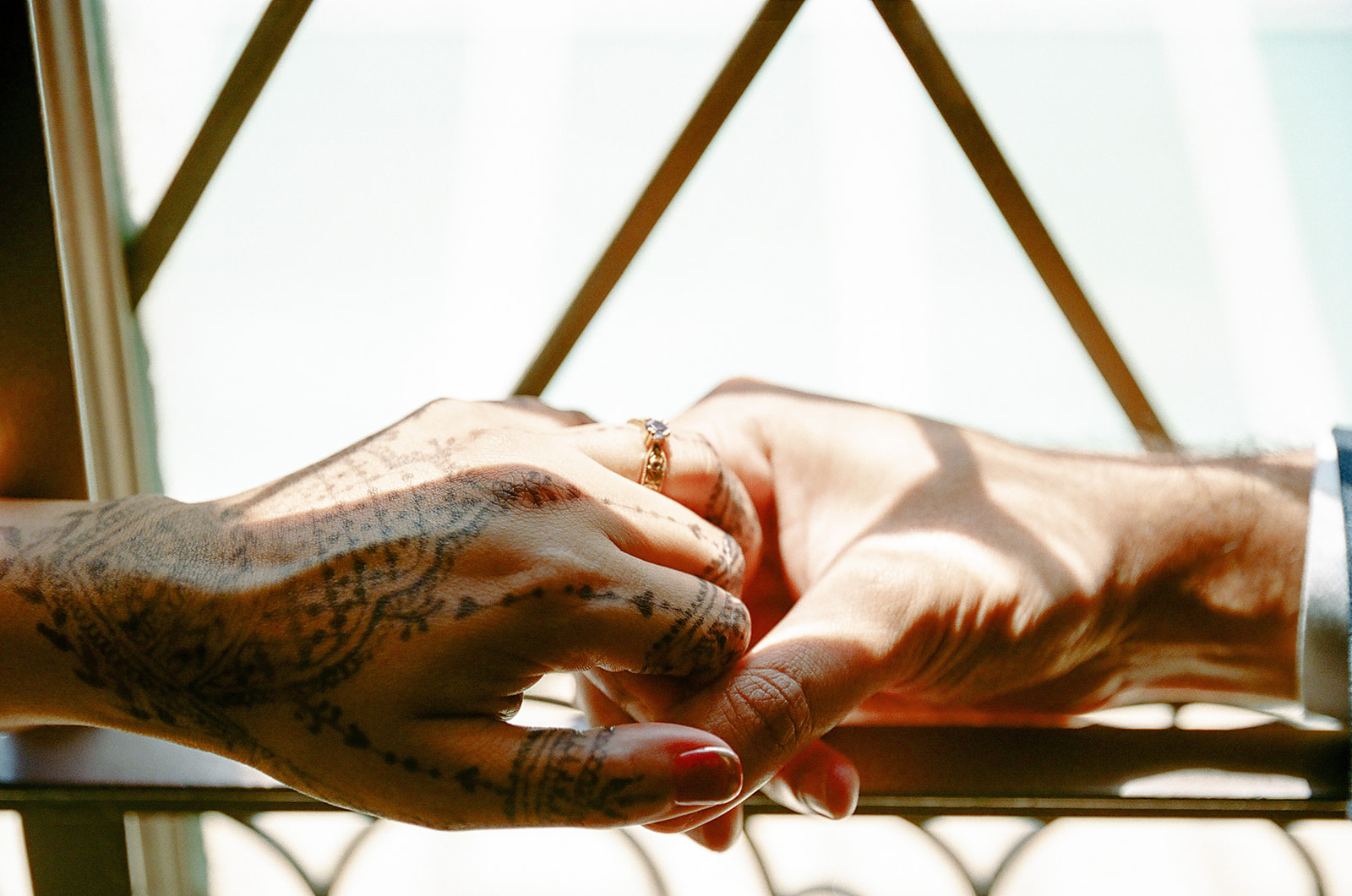 Close-up of the bride and groom holding hands, showing her henna and wedding ring.