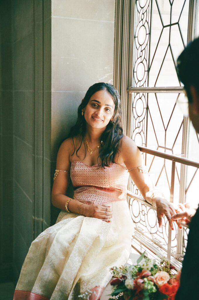 Newlyweds sitting by a decorative window and holding hands at San Francisco City Hall.