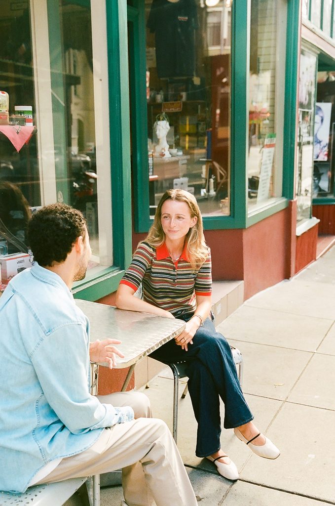 Engaged couple sitting across from each other at an outdoor café table in San Francisco's North Beach.