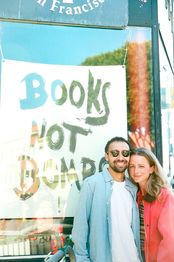 Engaged couple smiling outside City Lights Bookstore in San Francisco.