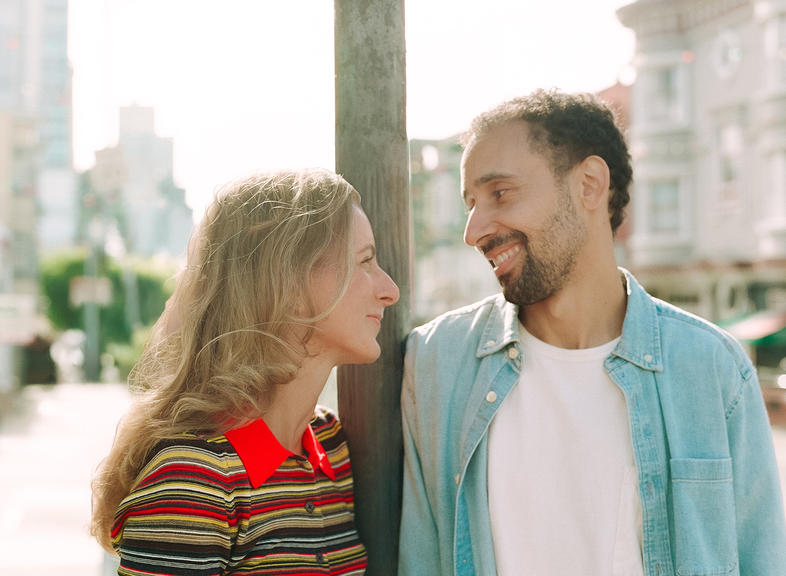 Close-up film portrait of an engaged couple smiling at each other in warm afternoon sunlight.