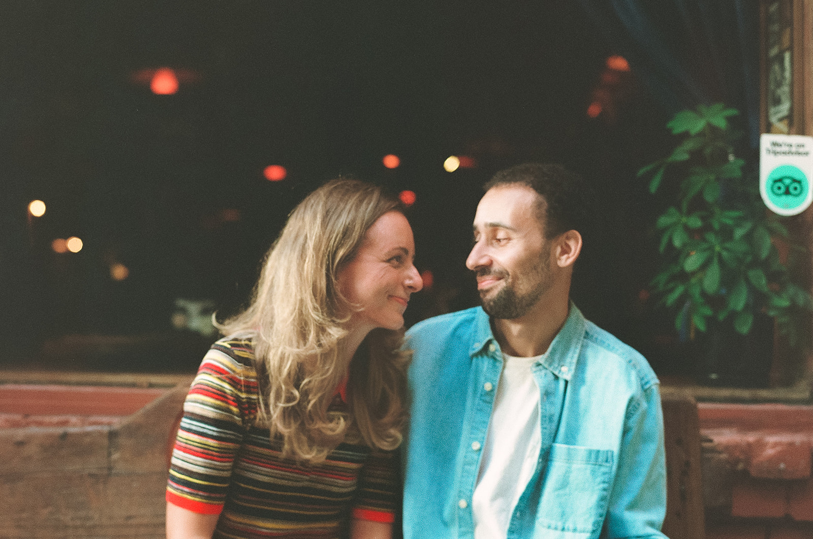 35mm film photo of a couple smiling at each other as they sit next to eachother. 
