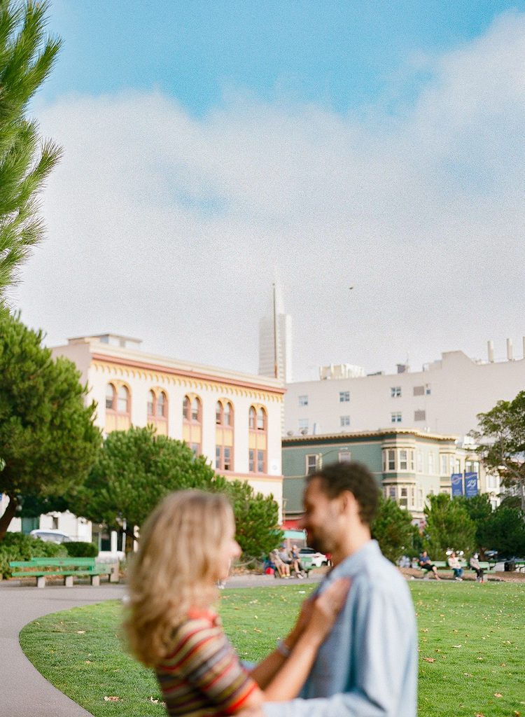 Couple posing together in Washington Square Park outside of Saints Peter and Paul Church for their SF engagement photos.