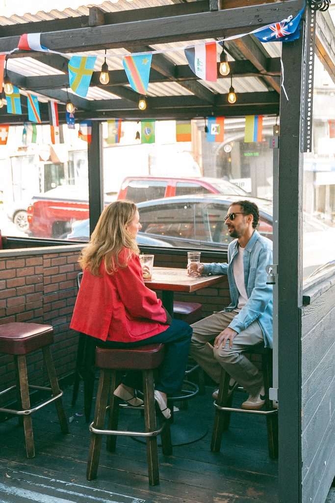 Engaged couple sitting across from each other at an outdoor café table in San Francisco's North Beach.