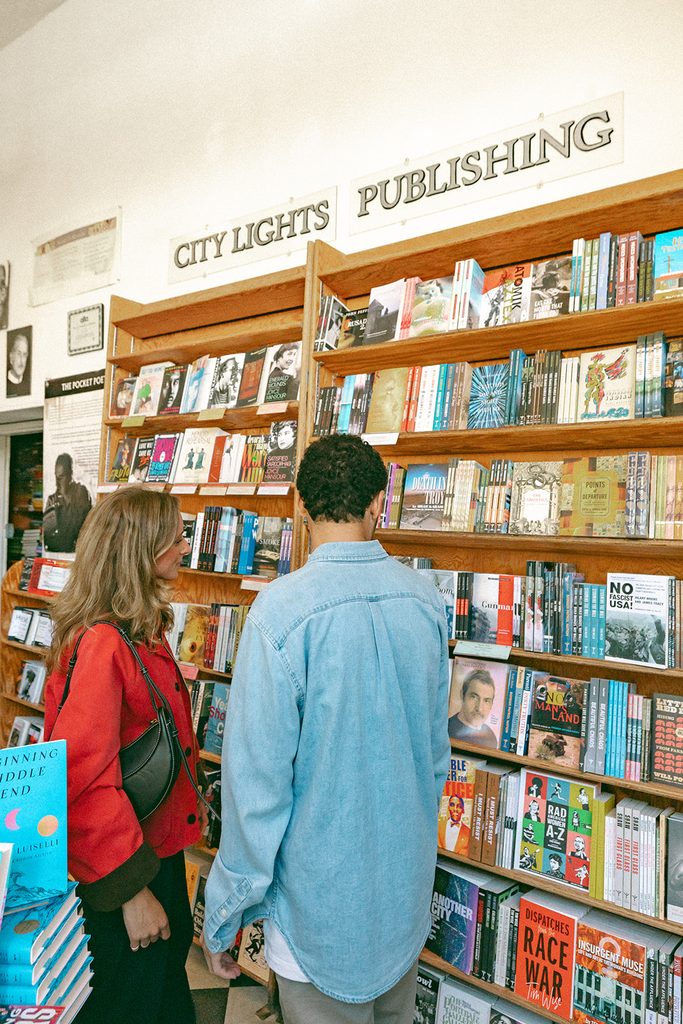 Couple browsing colorful bookshelves inside City Lights Bookstore during their engagement session.