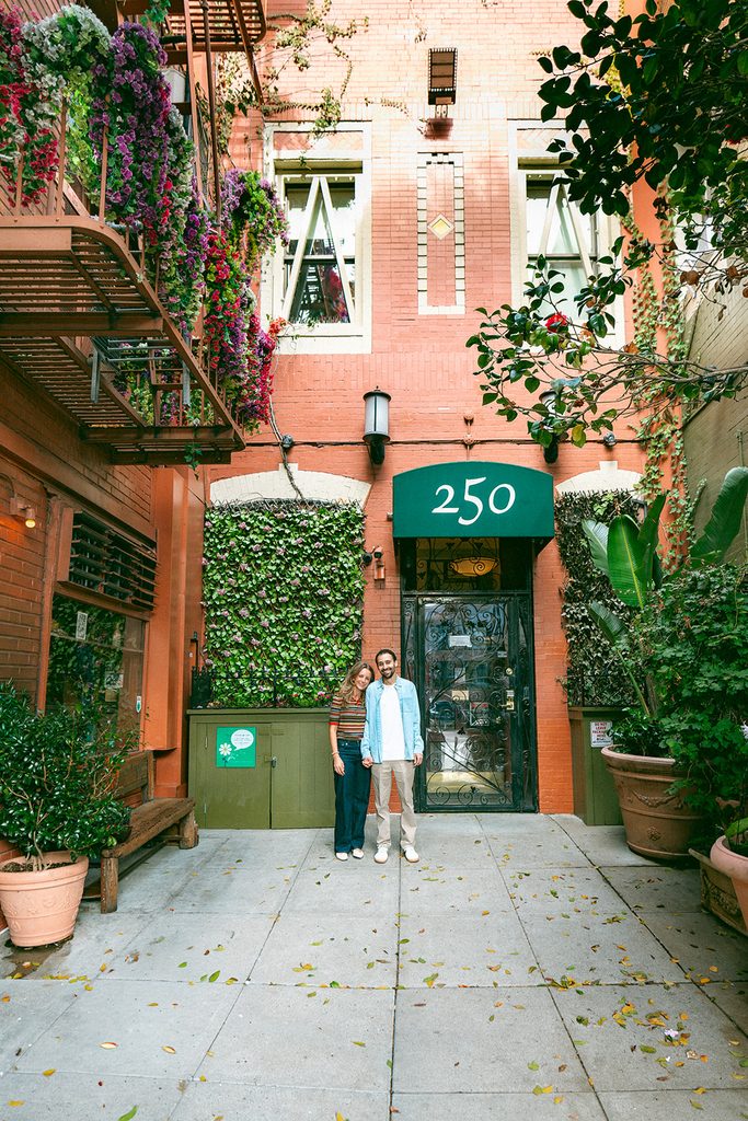 Couple standing together in a brick courtyard with flowering vines and greenery in North Beach.