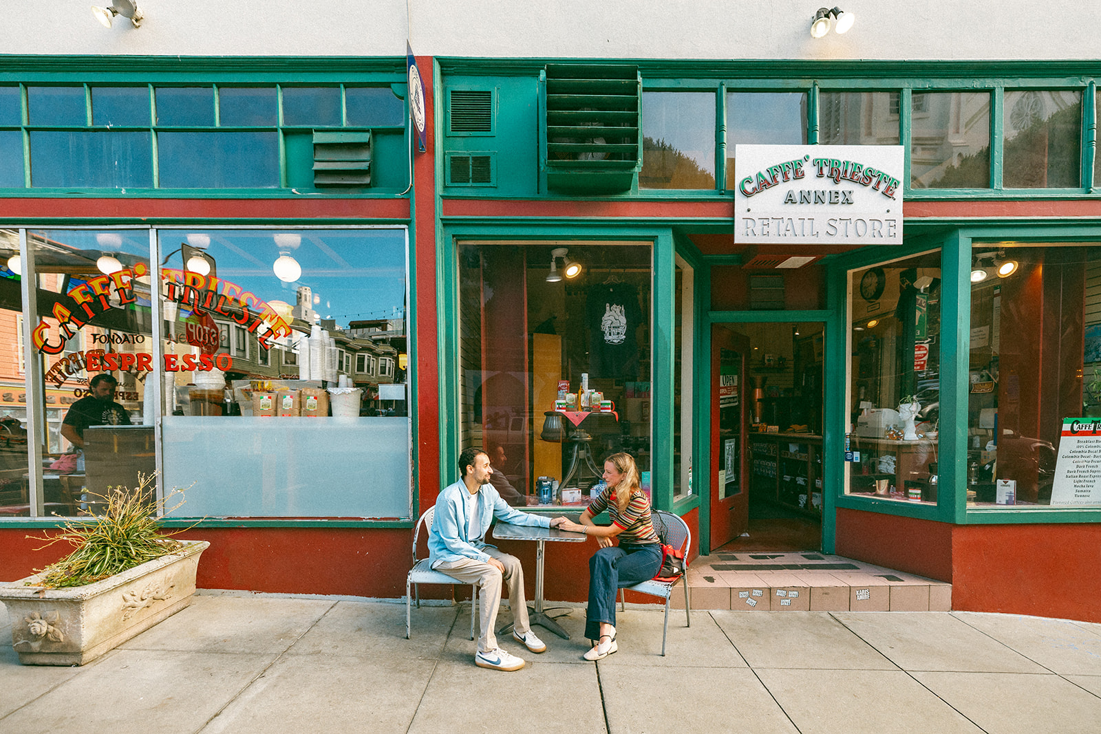 Couple sitting across rom one another outside of Caffe Trieste for their SF engagement photos in North beach.