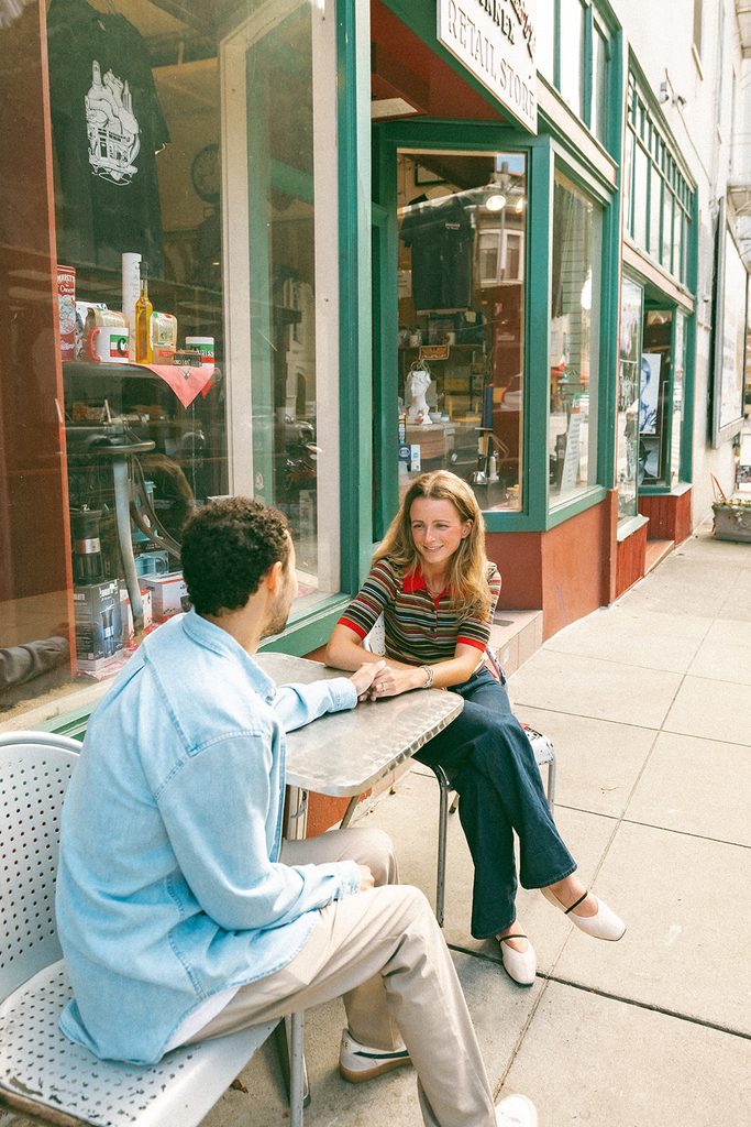 Couple sitting across rom one another outside of Caffe Trieste for their SF engagement photos in North beach.