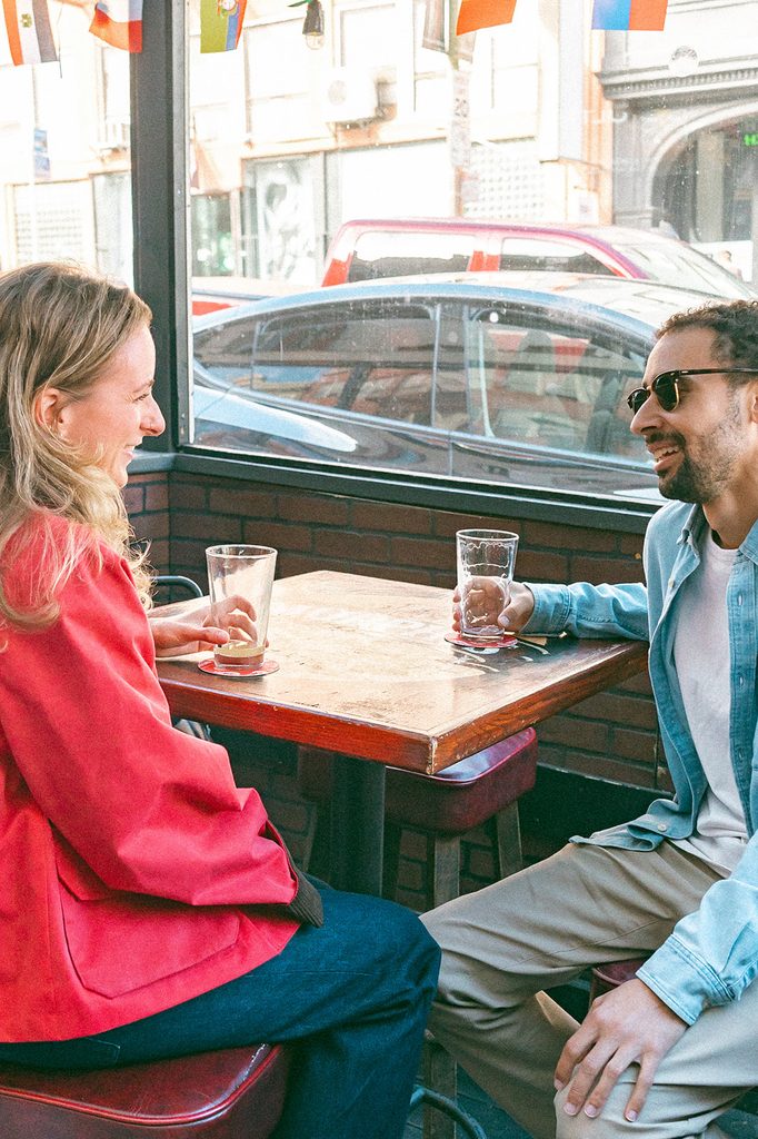 Engaged couple sitting across from each other at an outdoor café table in San Francisco's North Beach.