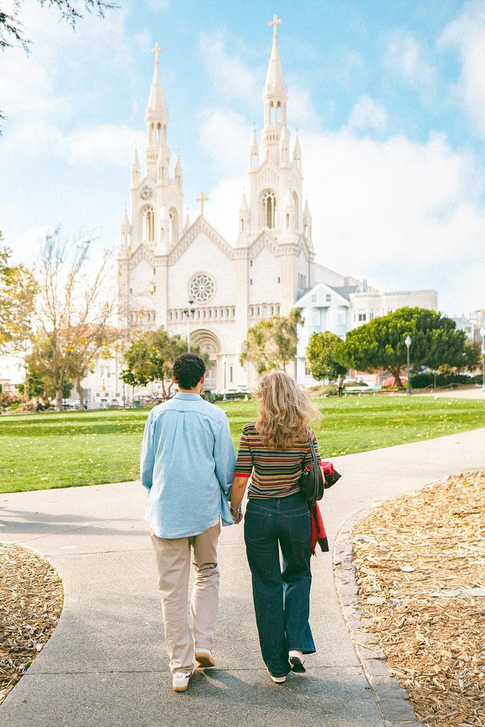 Couple walking hand in hand through Washington Square Park toward Saints Peter and Paul Church.