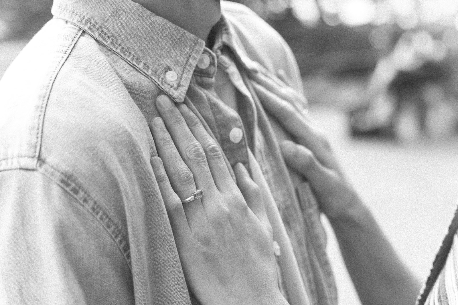 Close up black and white photo of a woman resting her hands on her fiancés chest showing her engagement ring.