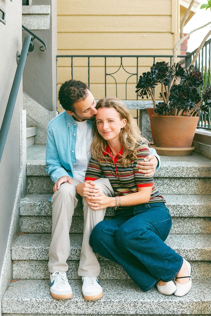 Couple cuddling on outdoor steps during their casual North Beach engagement session.