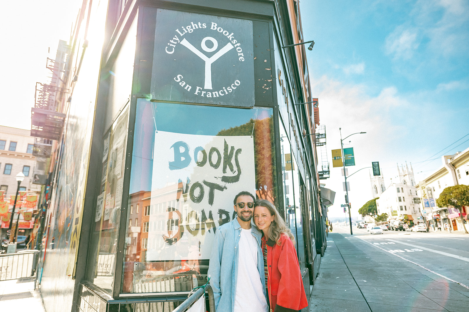 Engaged couple smiling outside City Lights Bookstore in San Francisco.